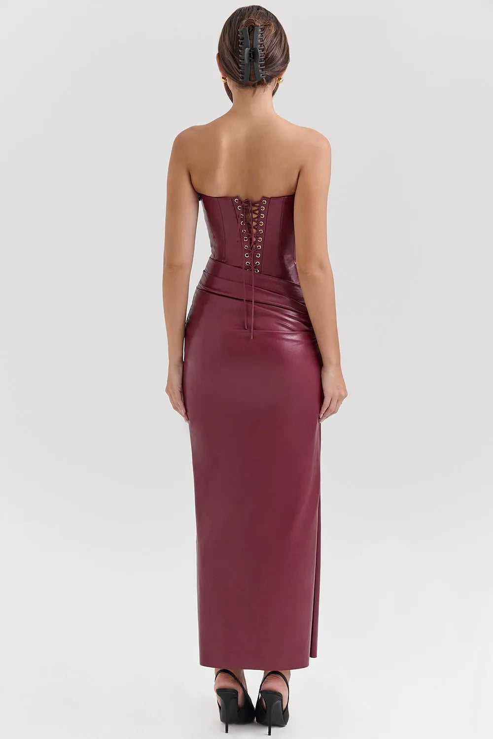 Mujer usando un vestido largo elegante en cuero vegano color vino, con corset estructurado sin tirantes y abertura lateral, ideal para gala o eventos de noche.